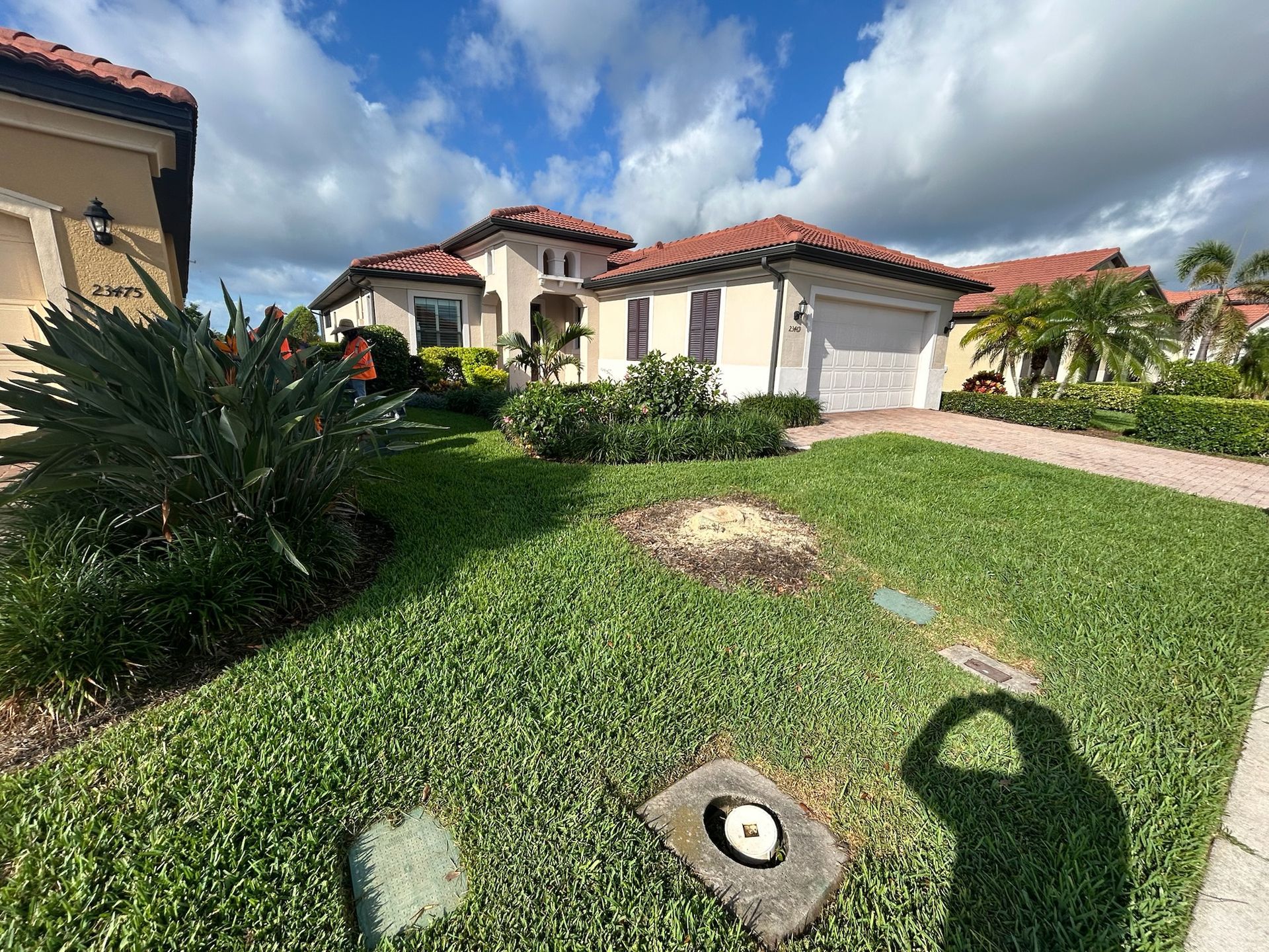 A beige house with a red-tiled roof, green lawn, and blue sky with clouds.