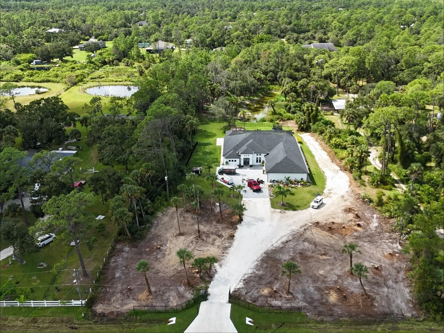 Aerial view of a home with a long driveway and partially cleared lots. Green trees surround the property.