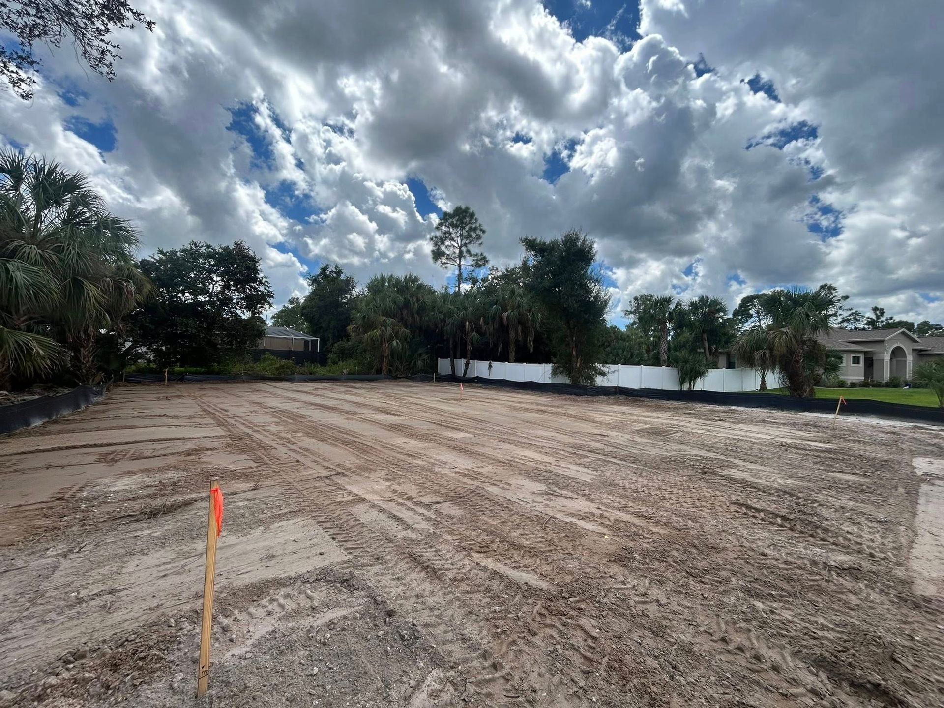 Cleared lot with dirt and tire tracks, cloudy sky, trees in the background, orange stake in the foreground.
