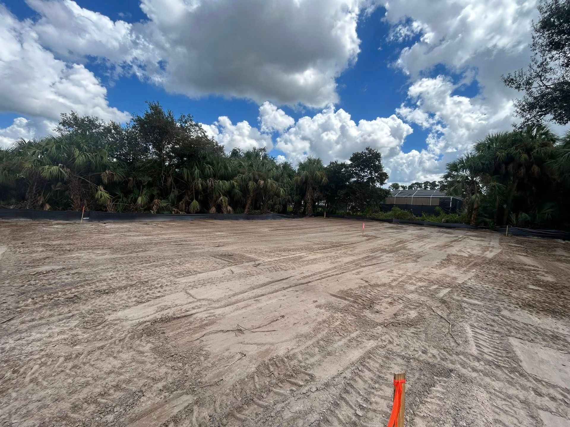 Cleared dirt lot under a cloudy blue sky, with trees in the background.