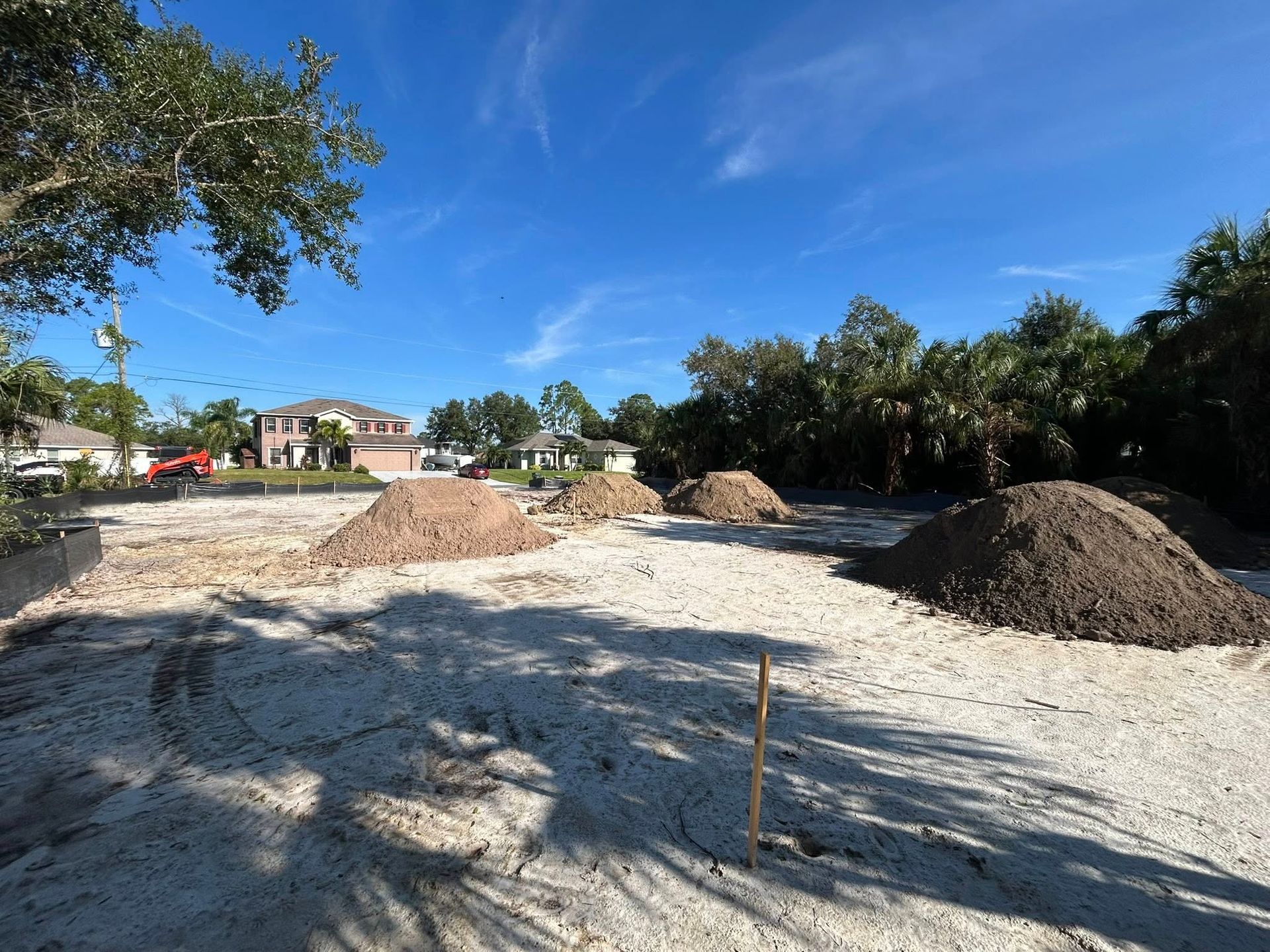 A construction site with piles of dirt on a white gravel base, under a clear blue sky.