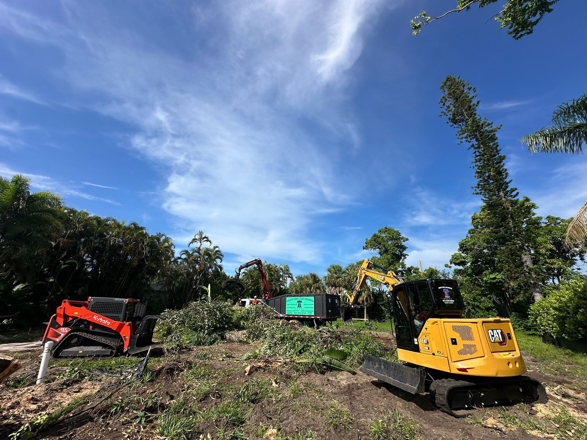 Construction site with machinery, clear blue sky, green foliage, and earth.