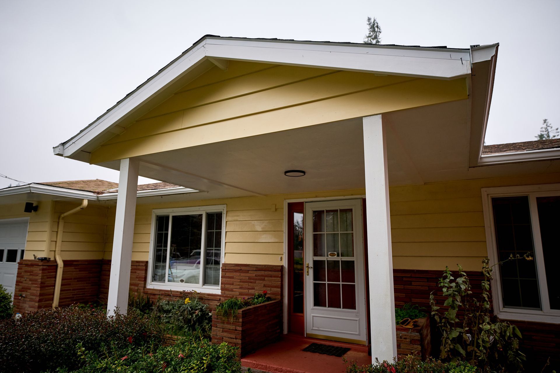 A yellow house with a porch and a red door.