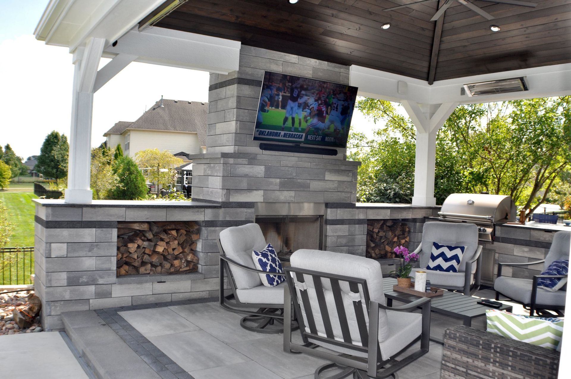 a patio with a fireplace, chairs, a table and a television