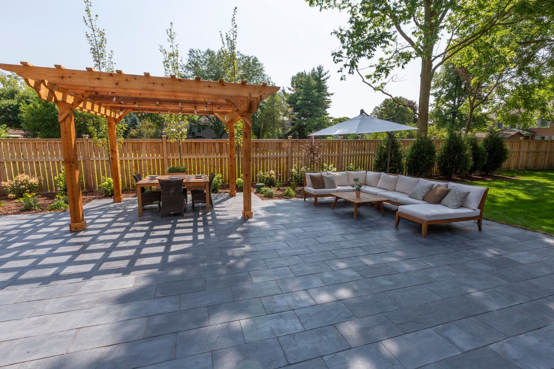 a patio with a pergola, couch, table and umbrella
