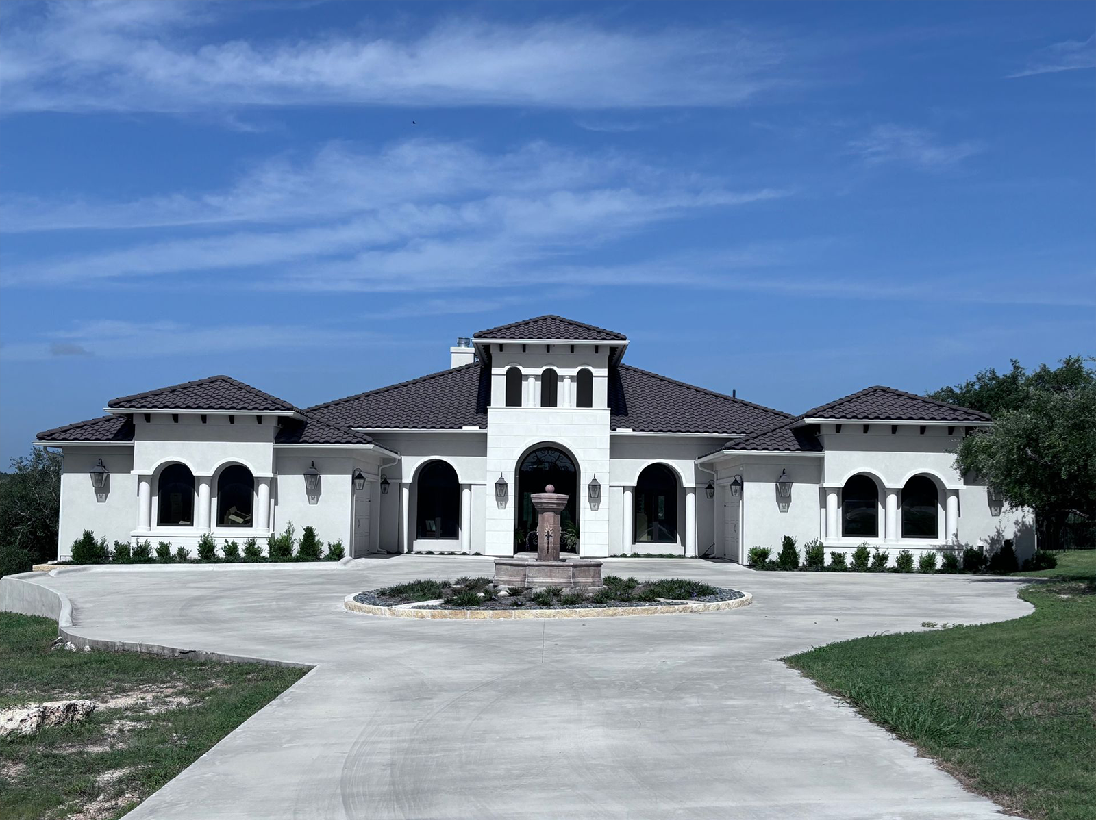 A large white house with a brown roof and a fountain in front of it.