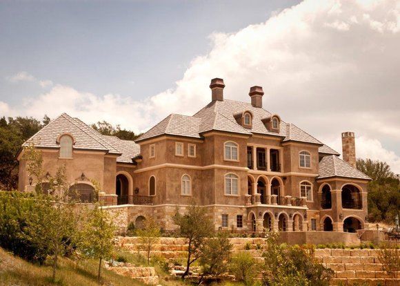 A large brick house is sitting on top of a hill surrounded by trees.