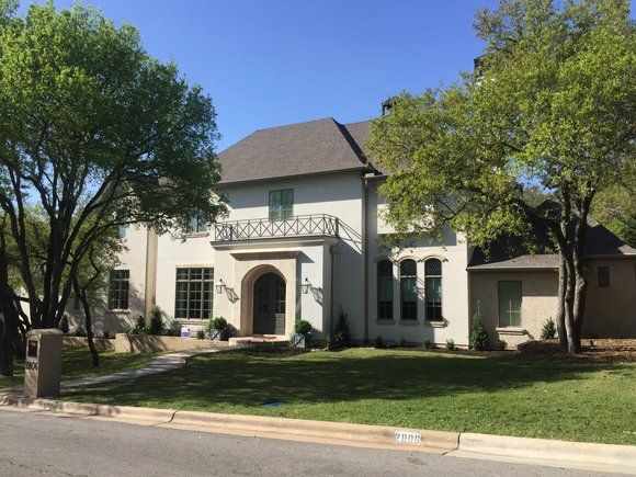 A large white house with a gray roof and trees in front of it