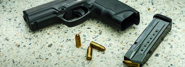 Black handgun with magazine and bullets on a speckled surface.