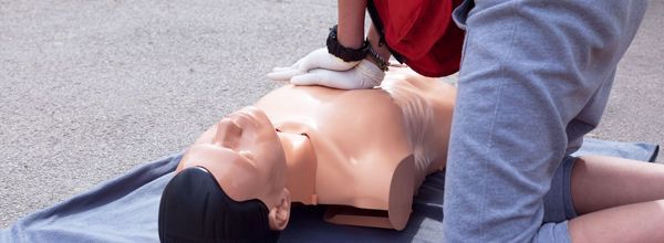 Person administering CPR on a mannequin outdoors.