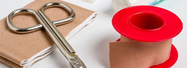 Scissors atop a package, next to a roll of red medical tape.