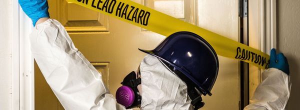 Person in protective suit, blue gloves, and mask blocks doorway with 