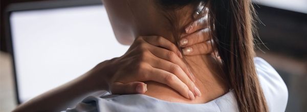 Woman holding her neck with pain. A laptop screen is visible in the background.