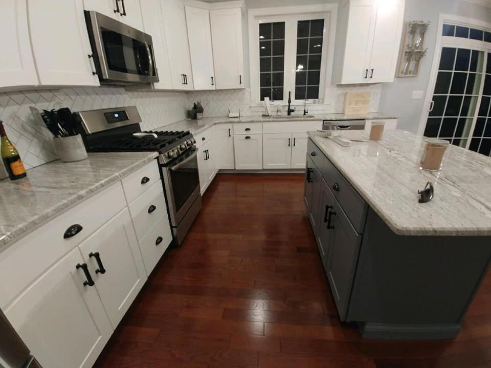 A modern kitchen with white cabinets, stainless steel appliances, and a gray island.