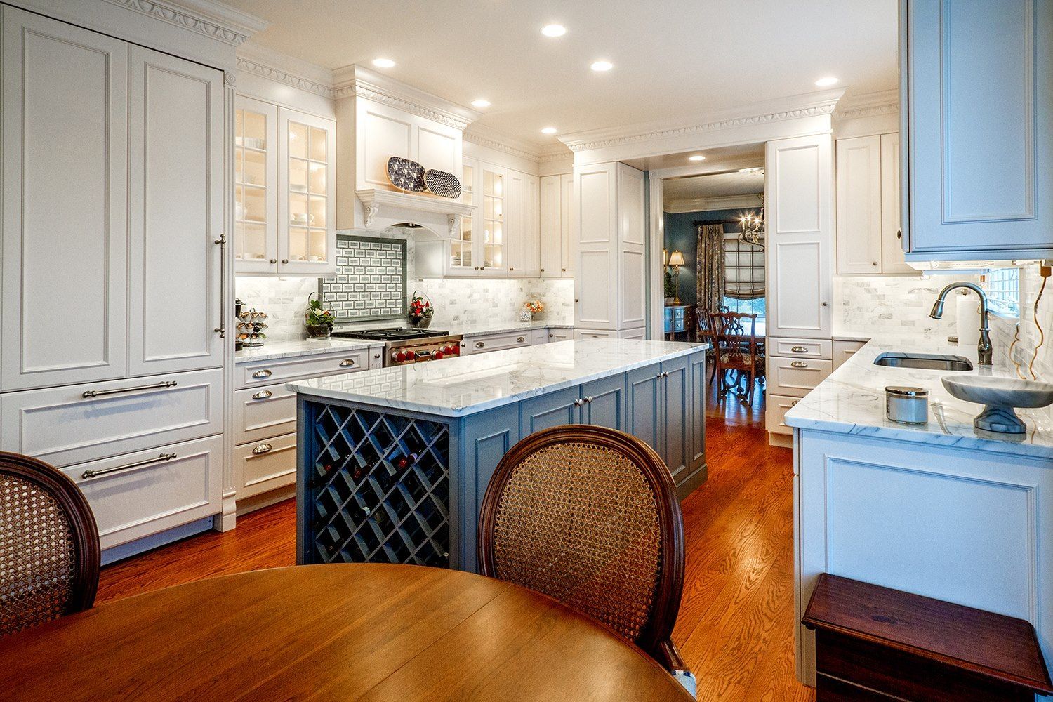 Elegant white kitchen with gray island, wine rack, and wood floor.