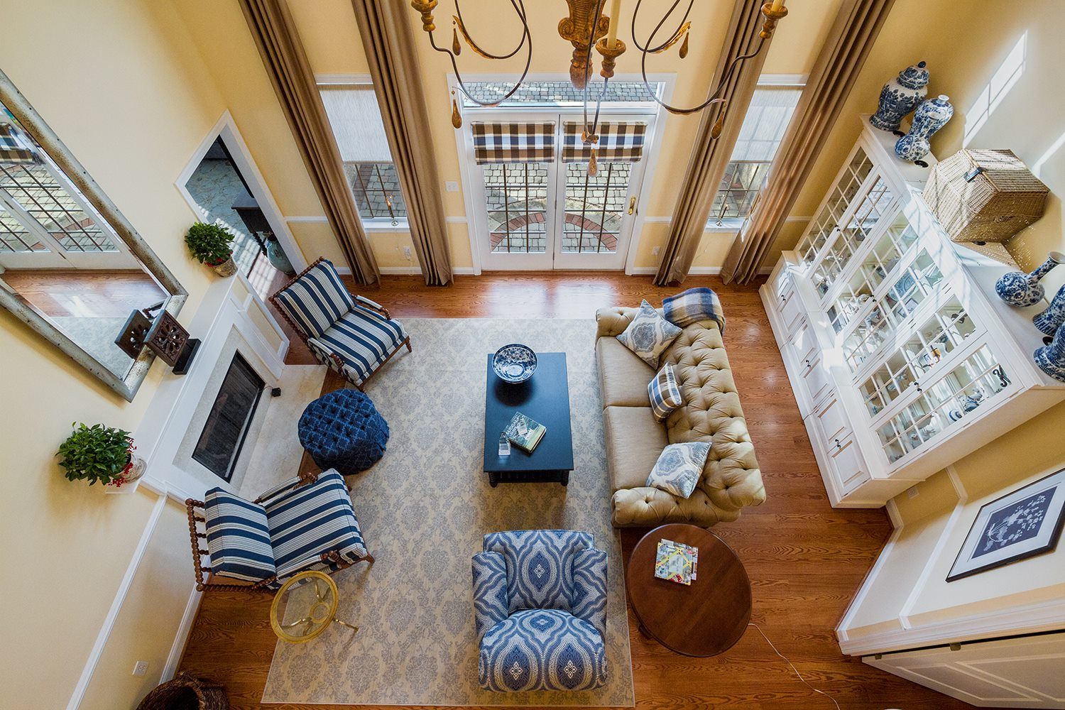 Overhead view of a living room with a tufted sofa, patterned chairs, a fireplace, and large windows.