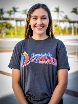 a young woman wearing a captain 's complete t-shirt is smiling for the camera .