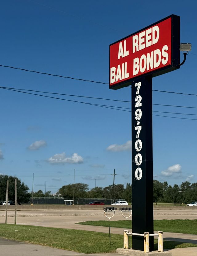 Al Reed Bail Bonds roadside sign with red lettering on a tall black pole under a blue sky.