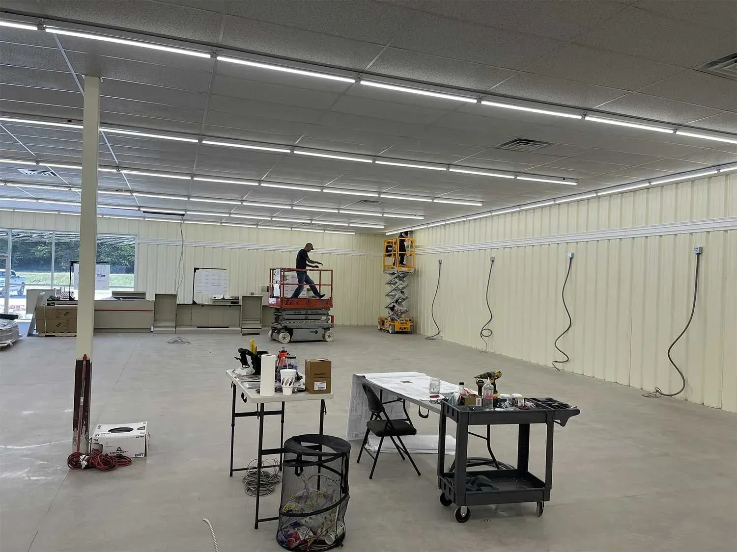 Interior of a building under construction, workers on lifts installing lighting.