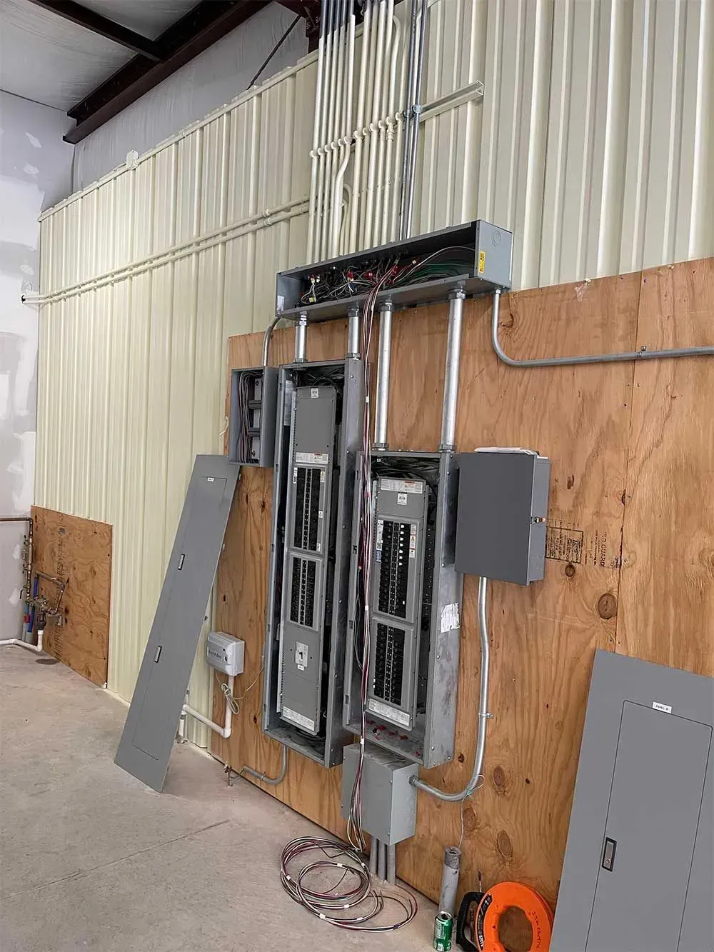 Electrical panel installation on a wooden wall in a building. Panels are gray, wiring is visible.