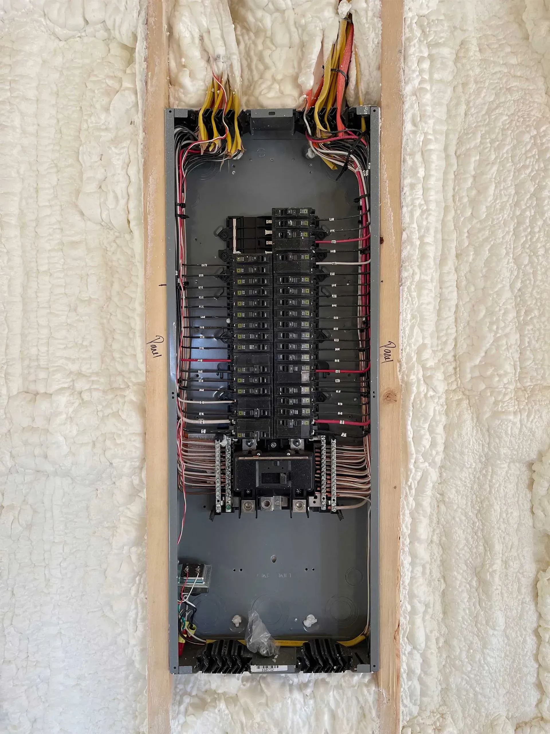 Electrical panel with multiple circuit breakers, wiring, and insulation in a wall cavity.
