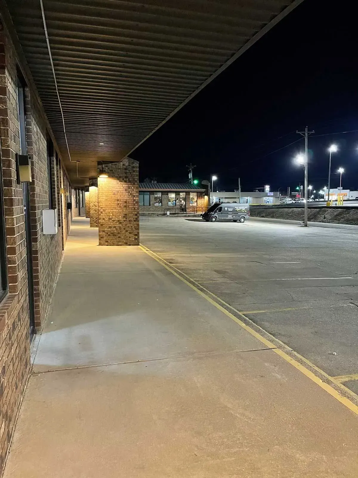 Exterior of a brick building with a covered walkway at night, streetlights illuminating an empty parking lot.