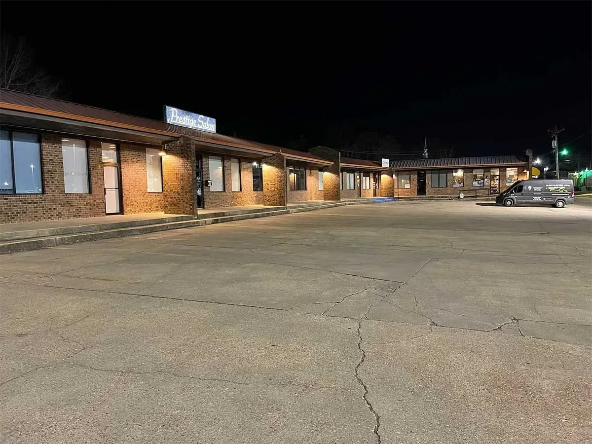 A nighttime view of a single-story brick building with a sign lit up, and a large empty parking lot.