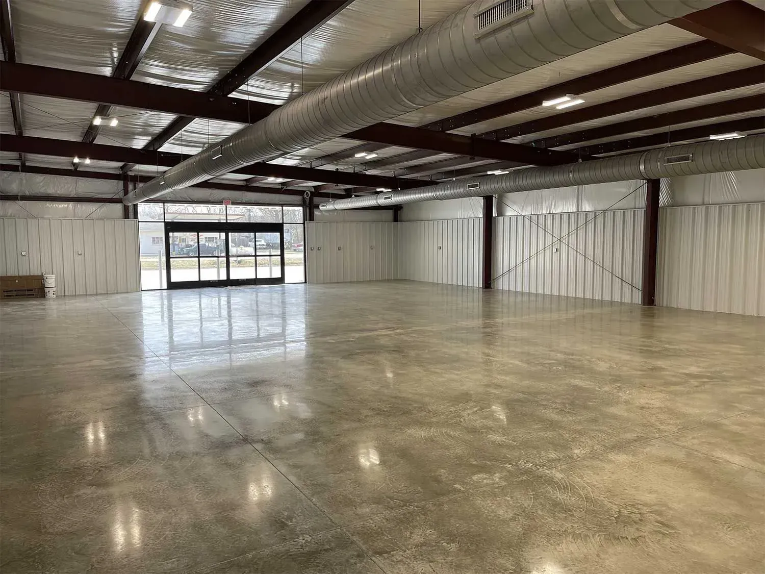 Empty warehouse interior with polished concrete floor, metal beams, and glass doors.