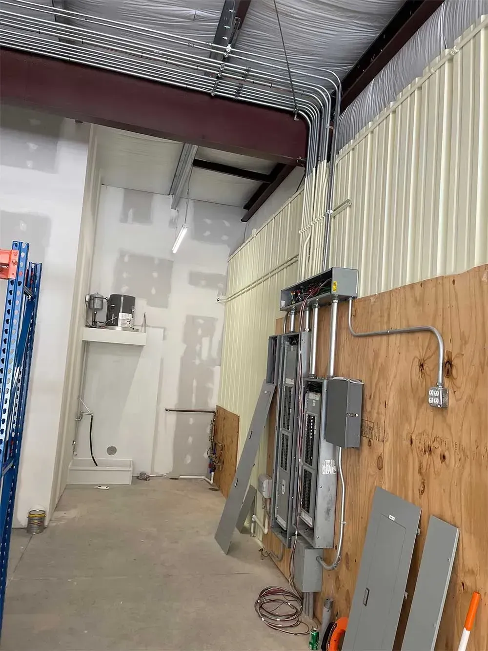 Interior view of an industrial space with electrical wiring and panels mounted on a plywood wall.