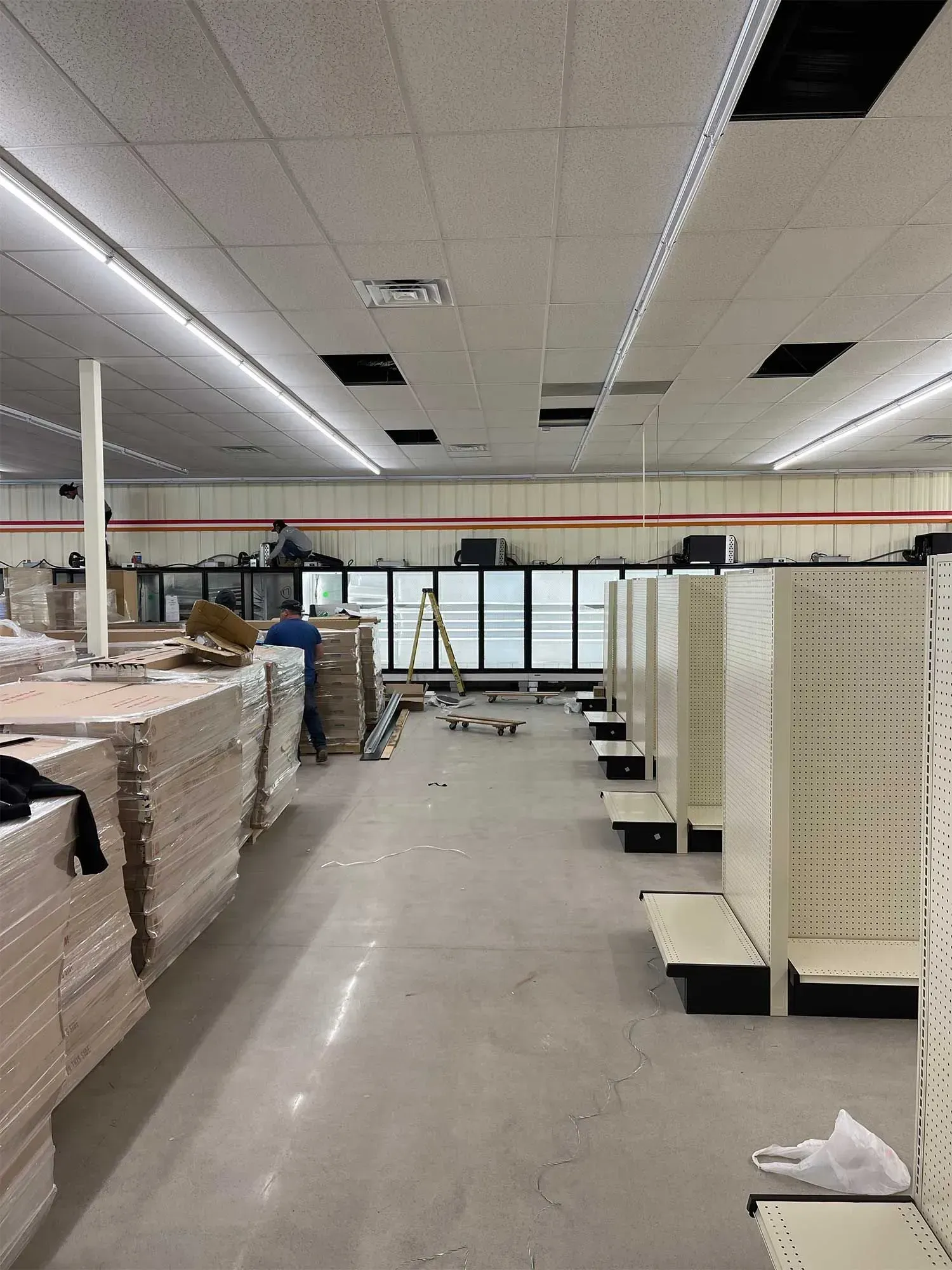 Interior of a store under construction with rows of shelves, workers, and display cases.