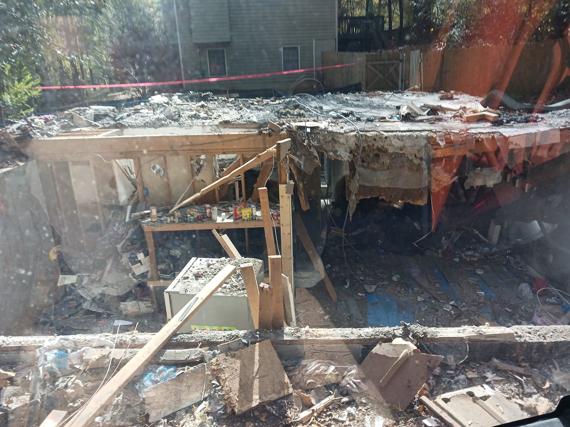 Debris-filled interior of a partially demolished building; wood beams, appliances, and rubble visible.