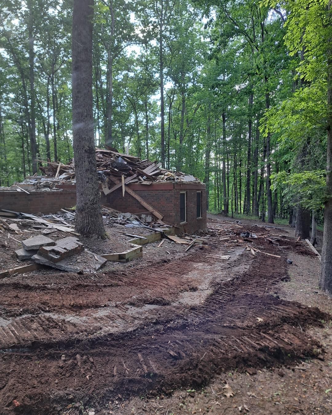 Demolished brick building in a forest setting; debris scattered on muddy ground.