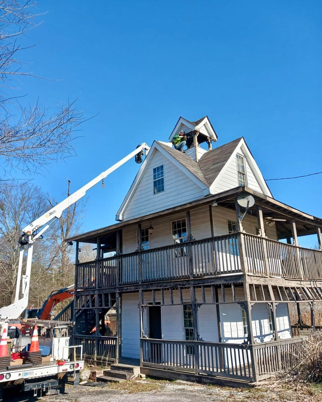 Workers in lift bucket working on the roof of a two-story white building under a clear blue sky.