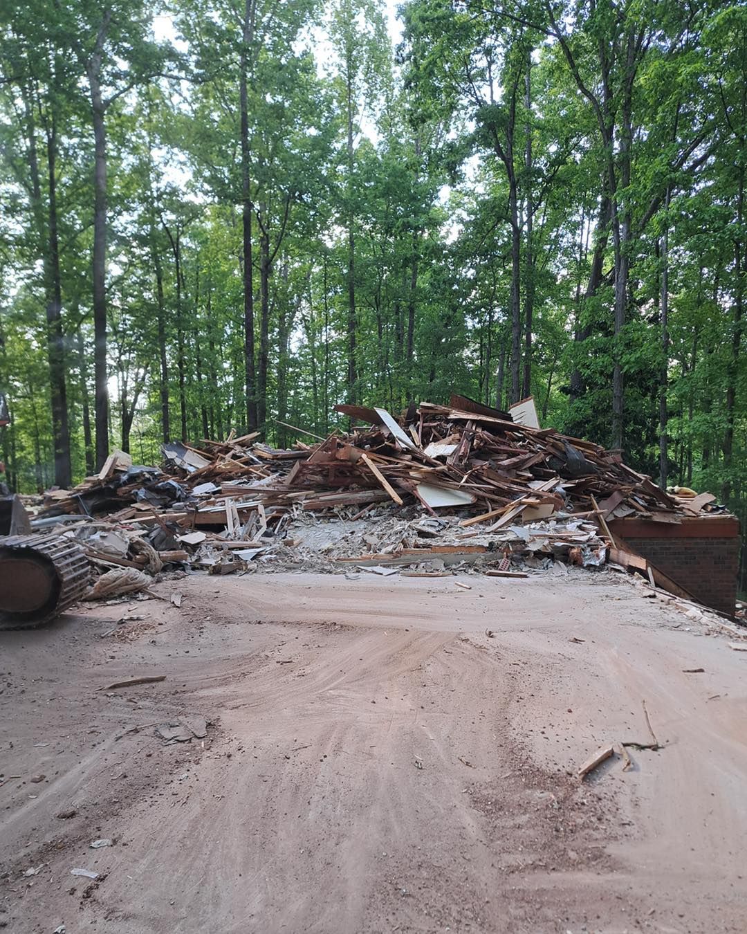 Pile of demolished debris on a sandy surface, with trees in the background.