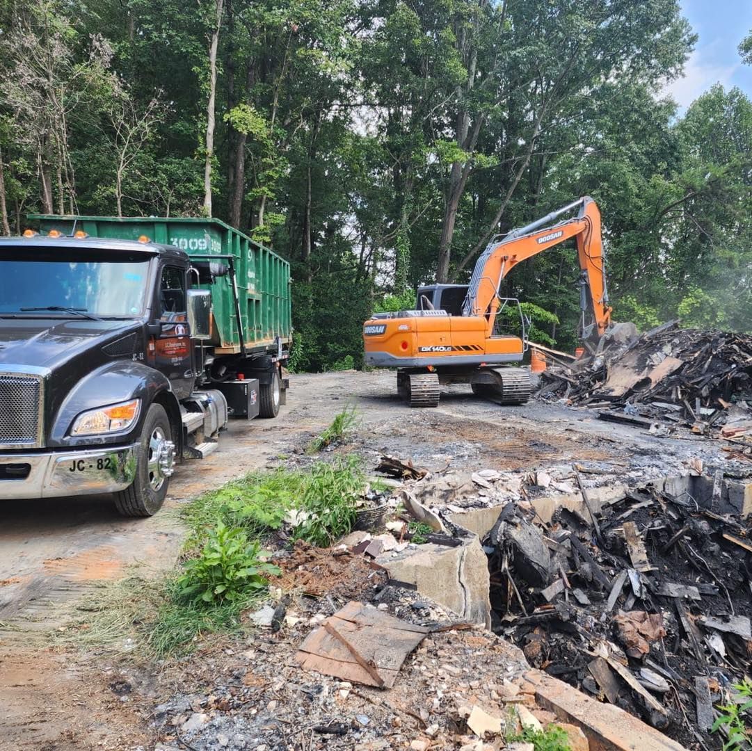 An excavator loading debris into a dump truck, both on a construction site. Trees in the background.
