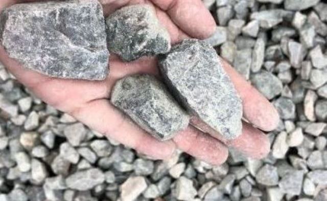 Hand holding gray rocks, surrounded by small gravel.