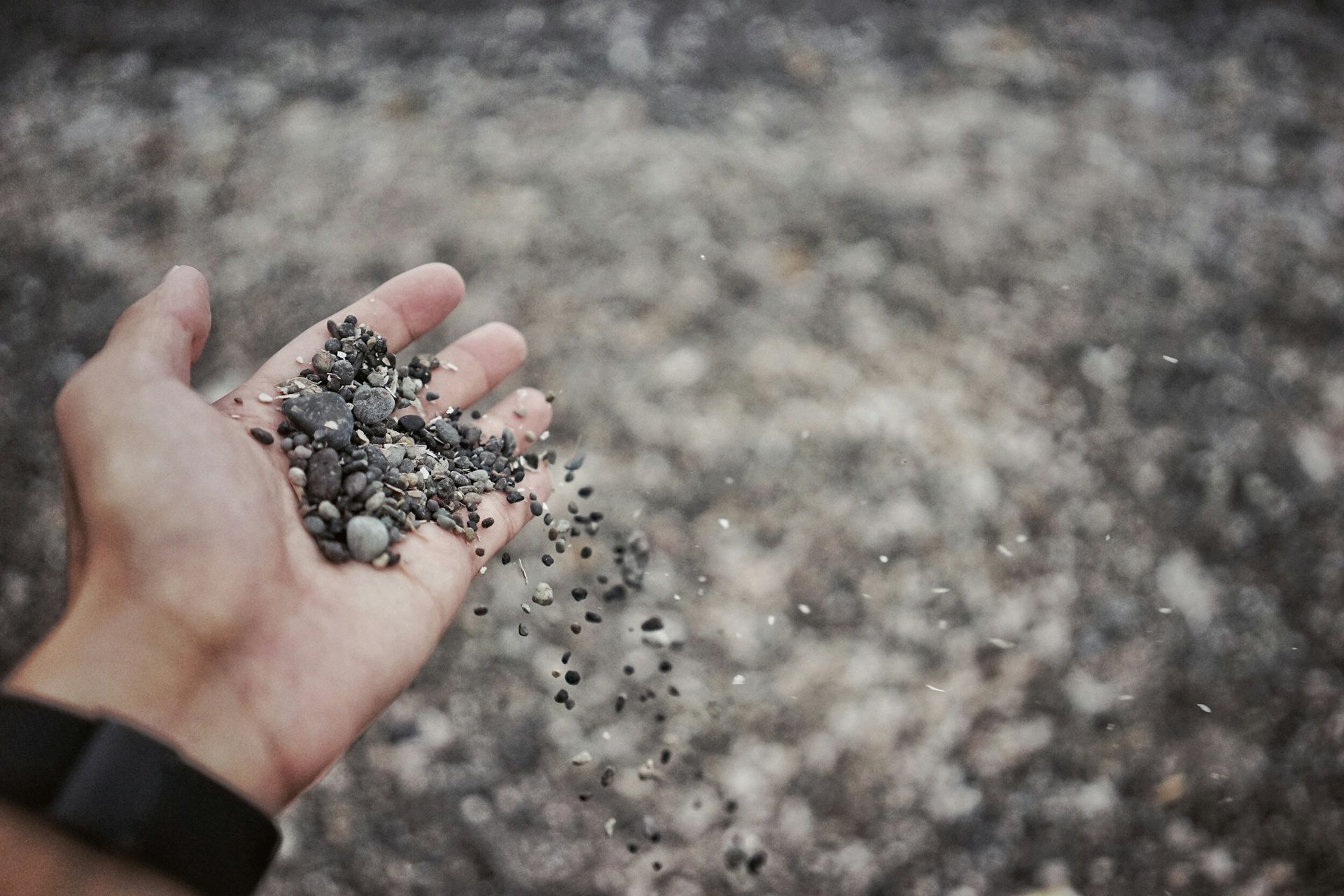 Hand holding small dark rocks, releasing them into the blurred background.