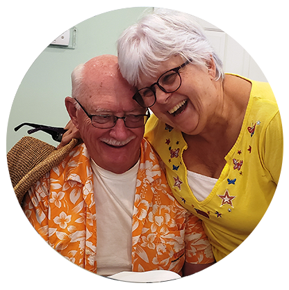 A woman in a yellow shirt is hugging an older man in an orange shirt