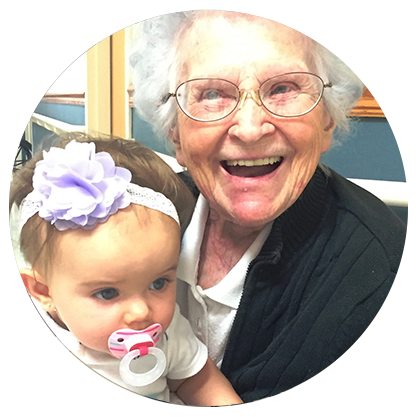 An elderly woman is holding a baby with a pacifier in her mouth