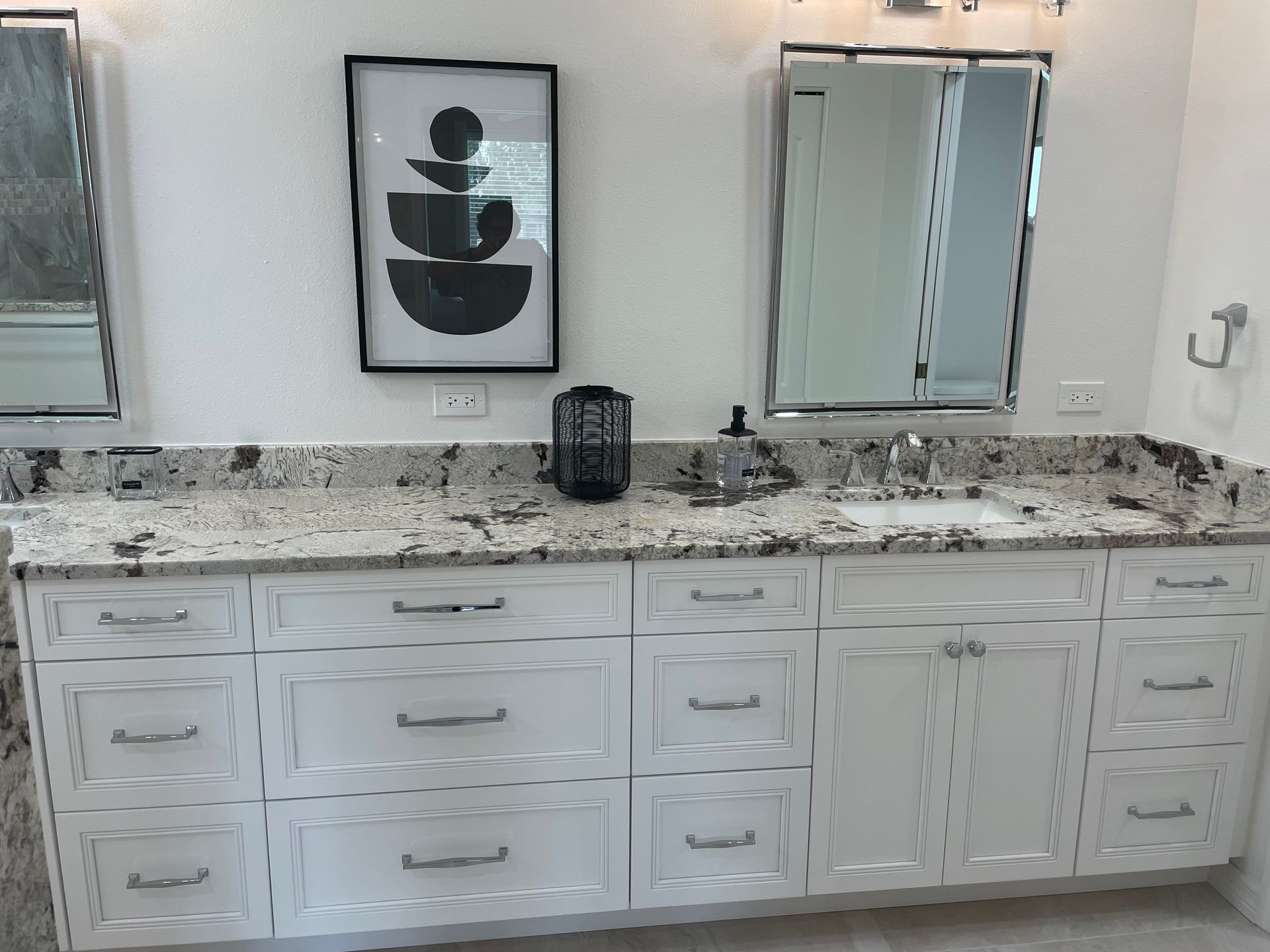 A bathroom with two sinks , two mirrors , and white cabinets.