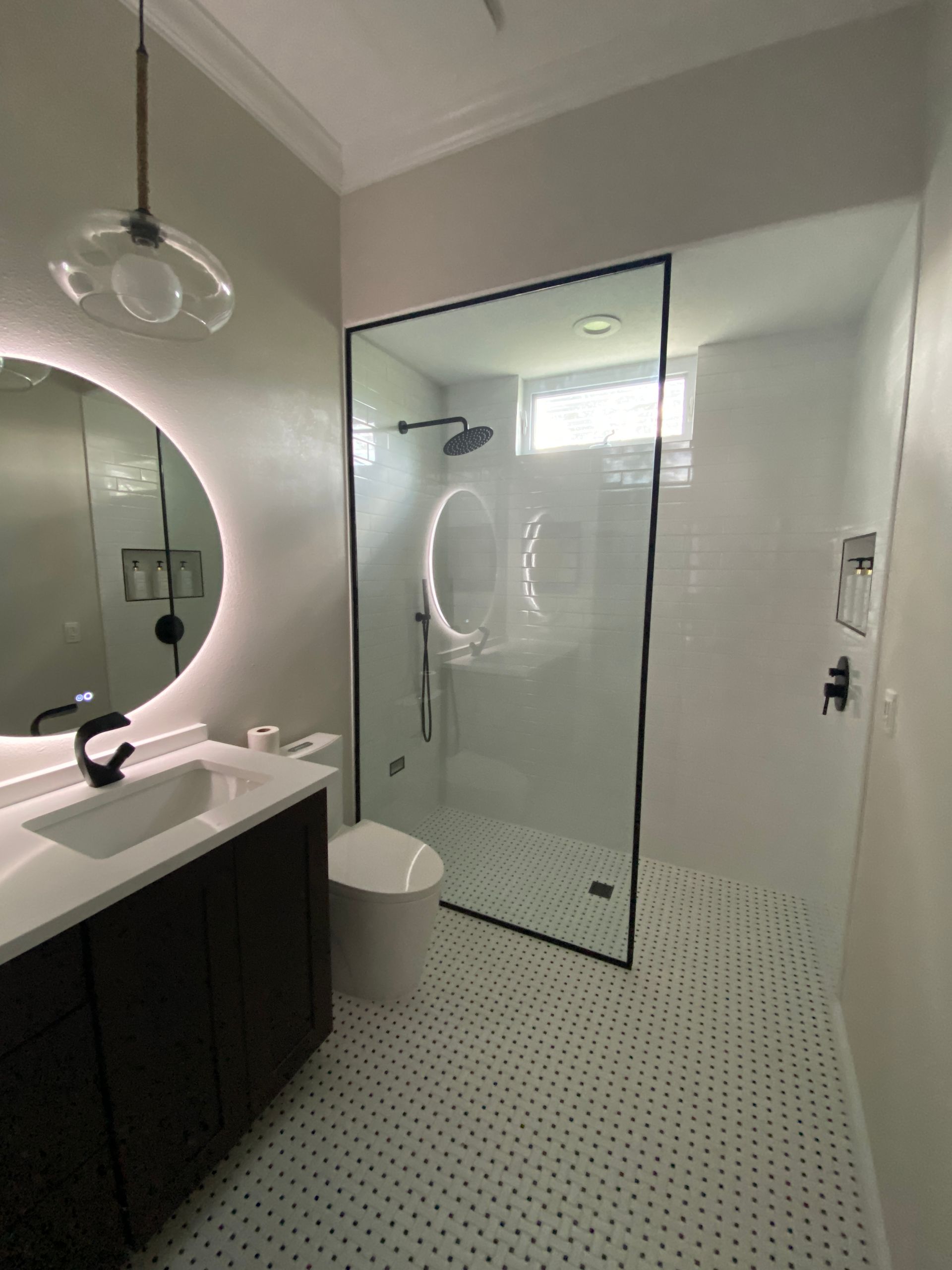 A bathroom with a walk in shower , sink , toilet and mirror.