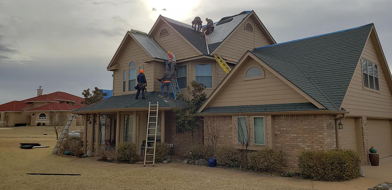 Roofers on a house under cloudy sky. Ladders and tools visible.