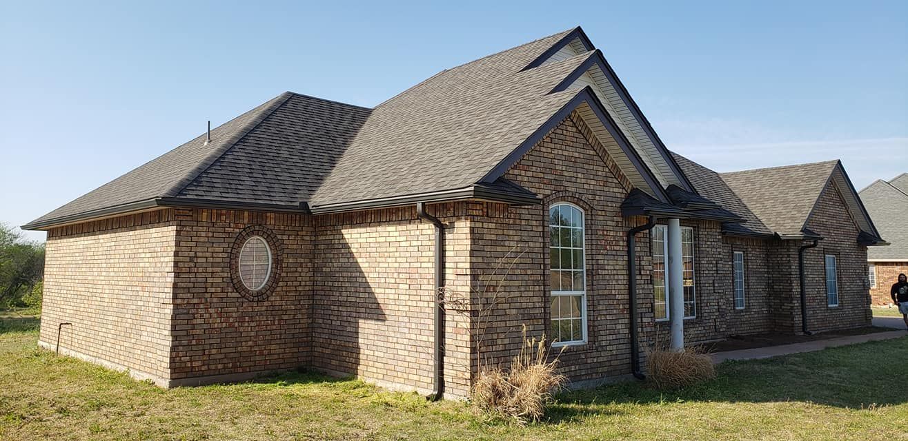 A brick house with a dark roof on a grassy lot, under a blue sky.