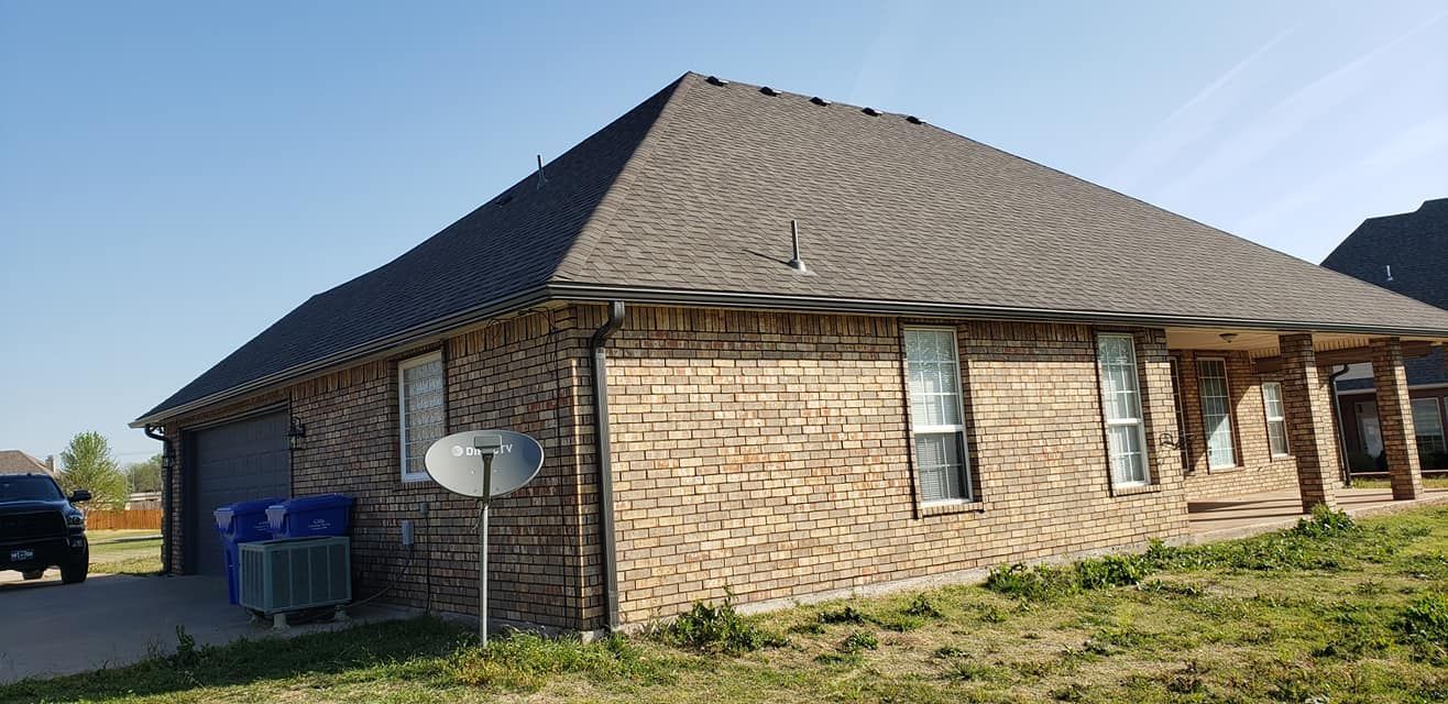 Brick house with dark roof, blue sky, and satellite dish.