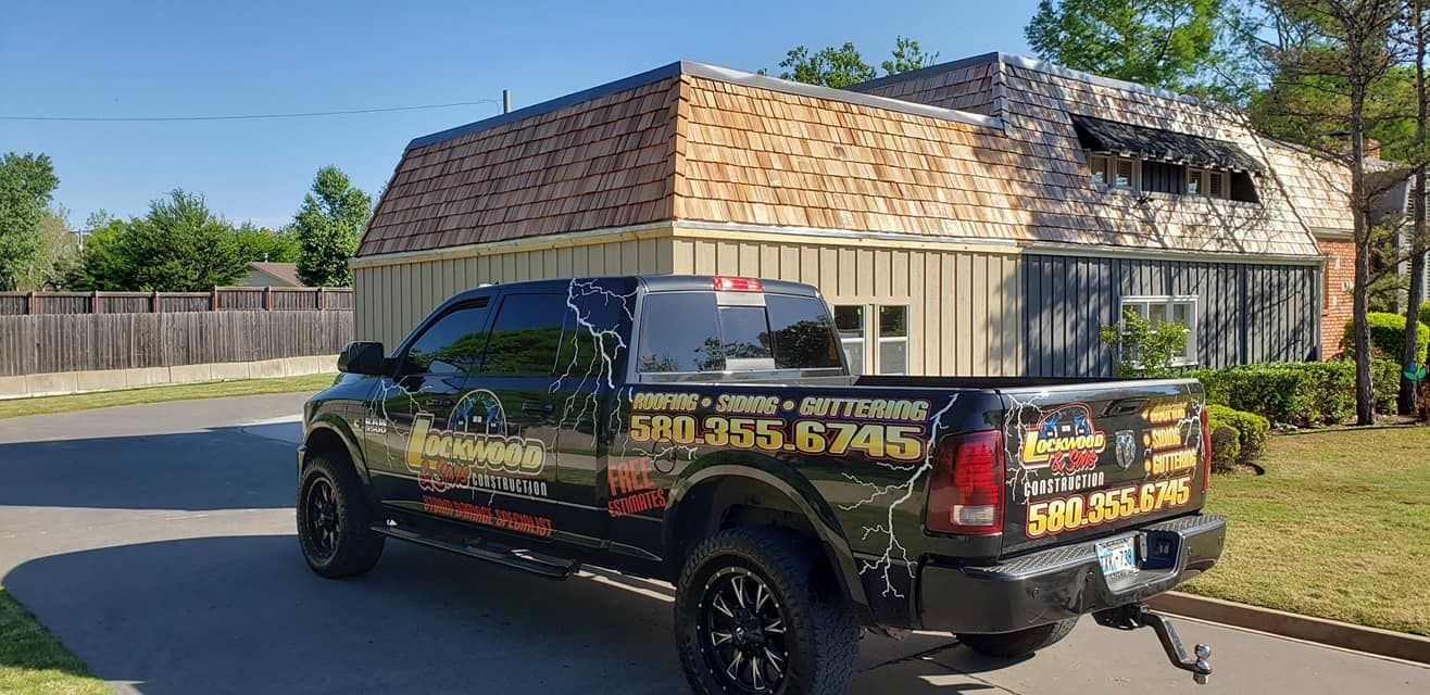 Black pickup truck with company logo parked in front of a building with roof repairs; sunny day.