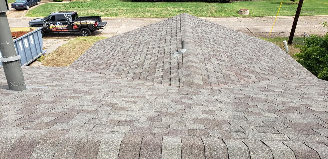 View of a roof with installed shingles, from above. A truck and dumpster are in the background.