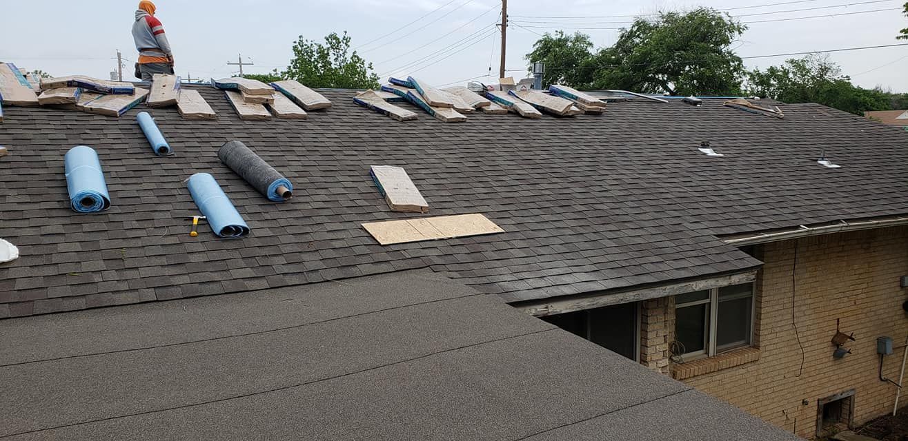 A roof partially stripped of shingles, with blue rolls and a worker visible.