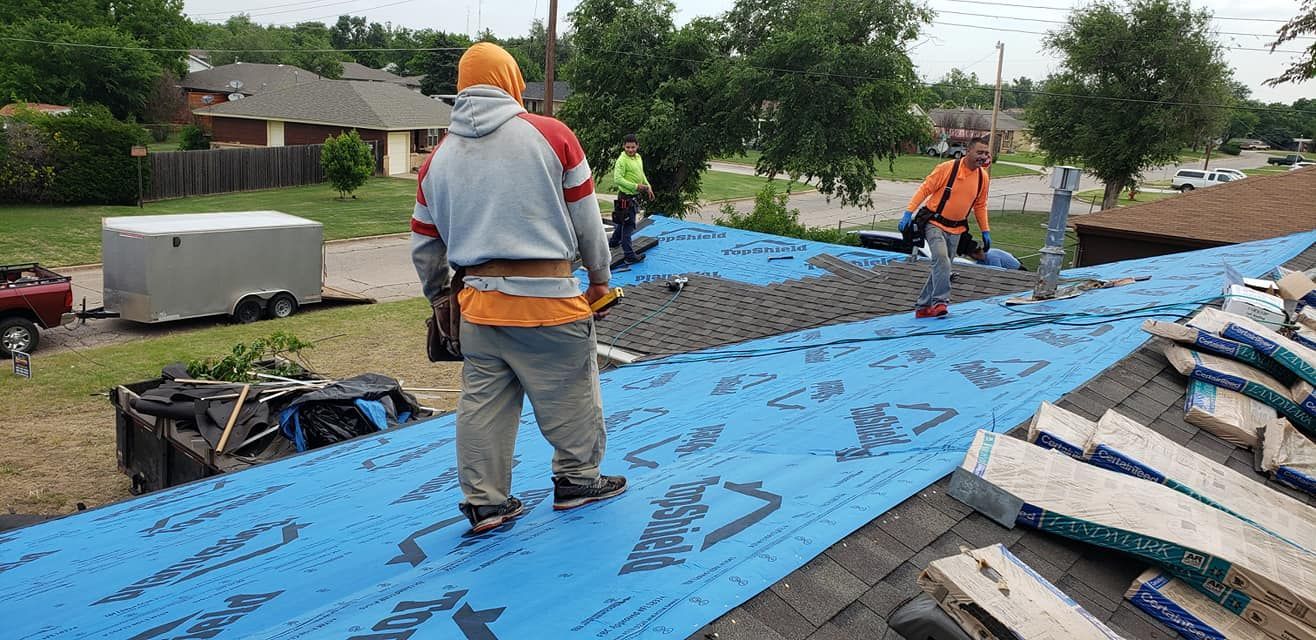 Roofers working on a roof, with blue tarp and tools. Overcast day.