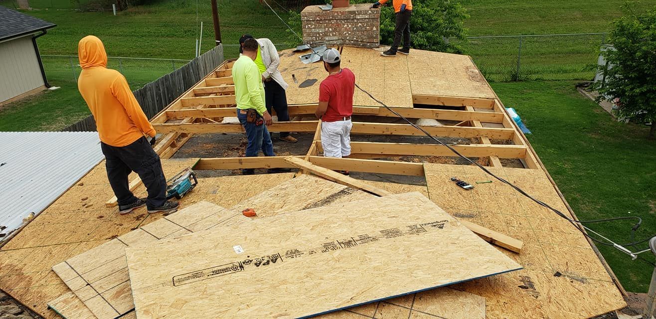 Roofers working on a house roof.  They are installing wooden panels and are wearing work clothes.