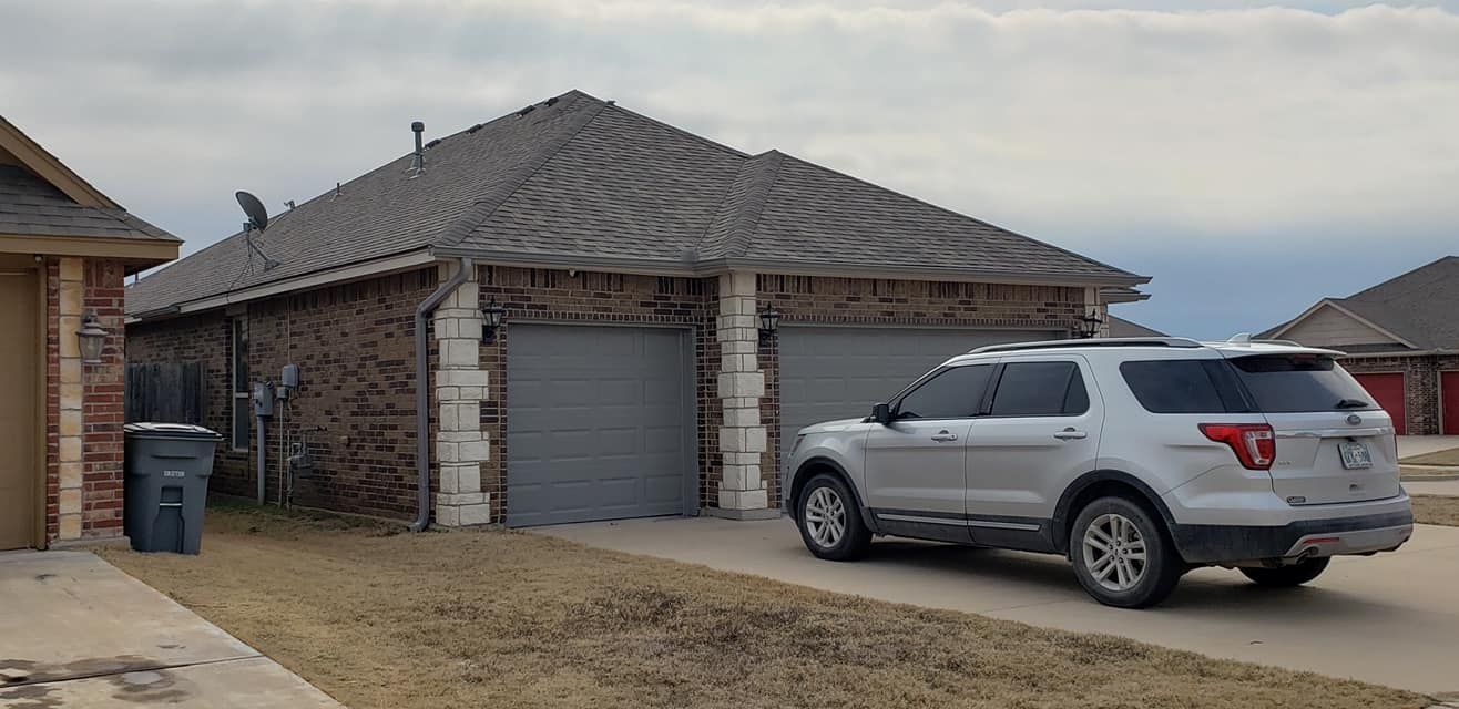 A silver SUV parked in front of a brick house with a gray roof and two garage doors.